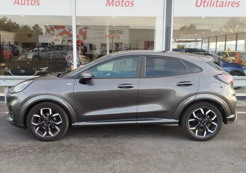 Profil droit d'un Ford Puma 1.0 EcoBoost gris métallisé avec jantes alliage noires et détails sportifs visibles.