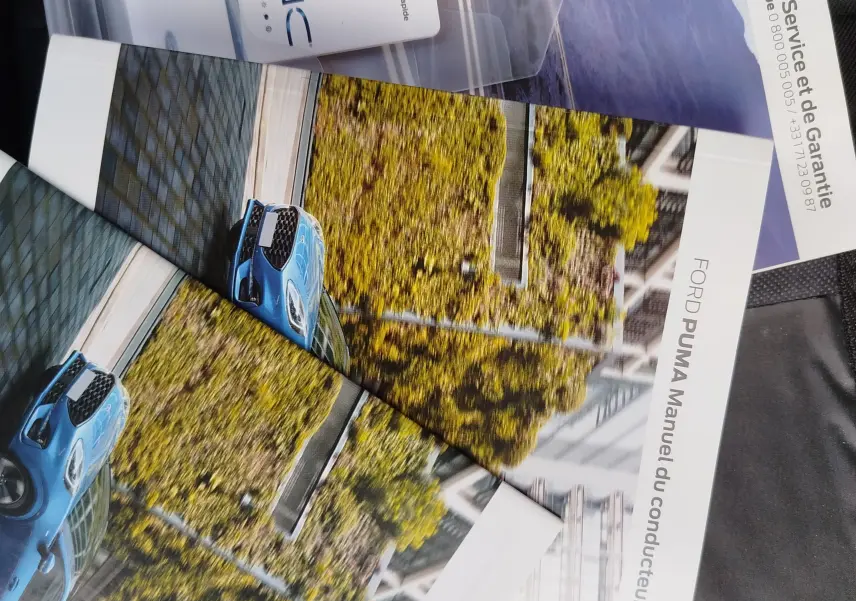 Vue 3/4 avant d'une Ford Puma bleue sur une route urbaine bordée d'arbres en automne.