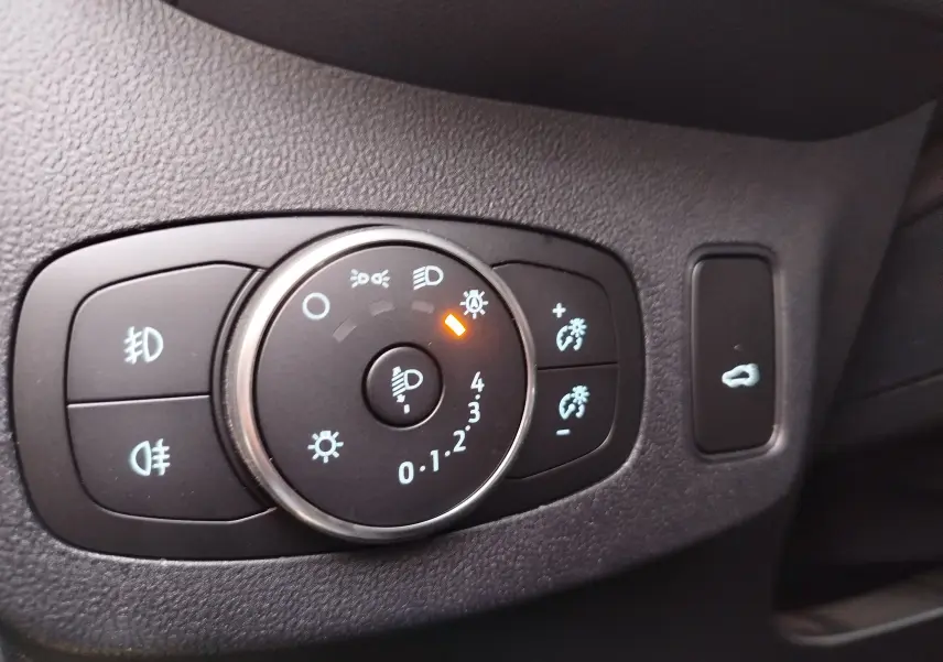 Gros plan sur le bouton de réglage des phares avec témoin orange, intérieur noir du Ford Puma 2020.