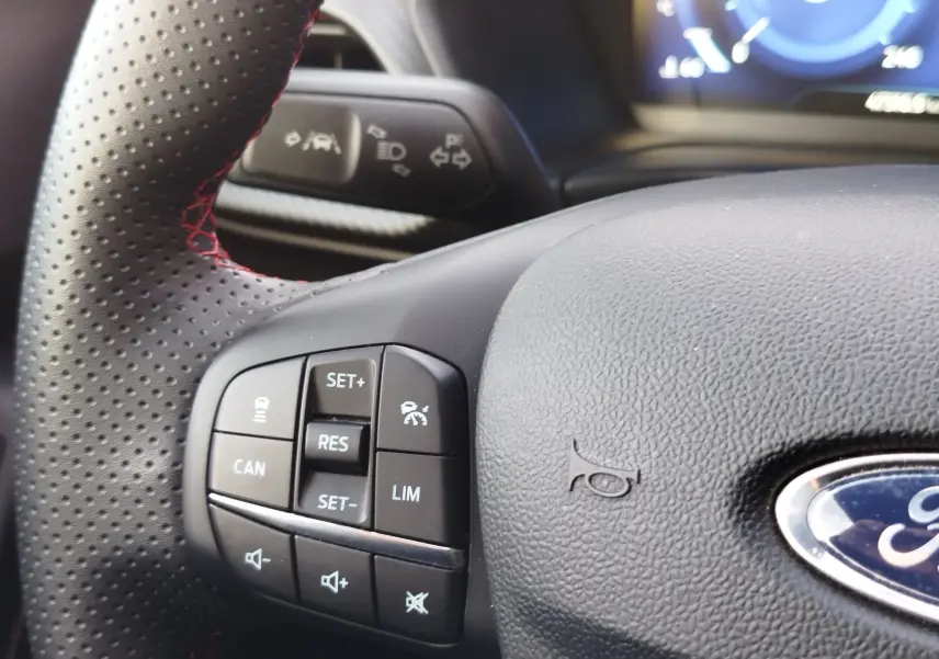 Gros plan sur le volant en cuir noir perforé avec surpiqûres rouges du Ford Puma 2020, montrant les commandes intégrées.