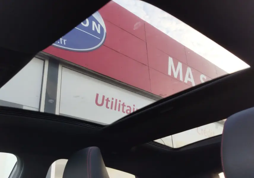 Vue intérieure du toit ouvrant panoramique du Ford Puma 1.0 EcoBoost gris avec sièges noirs et surpiqûres rouges.