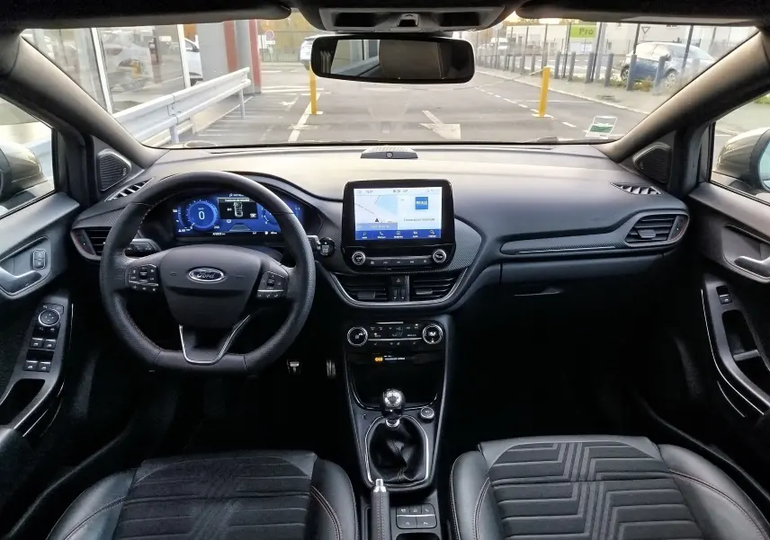 Vue intérieure avant du Ford Puma gris, tableau de bord moderne avec écran tactile et volant multifonction.
