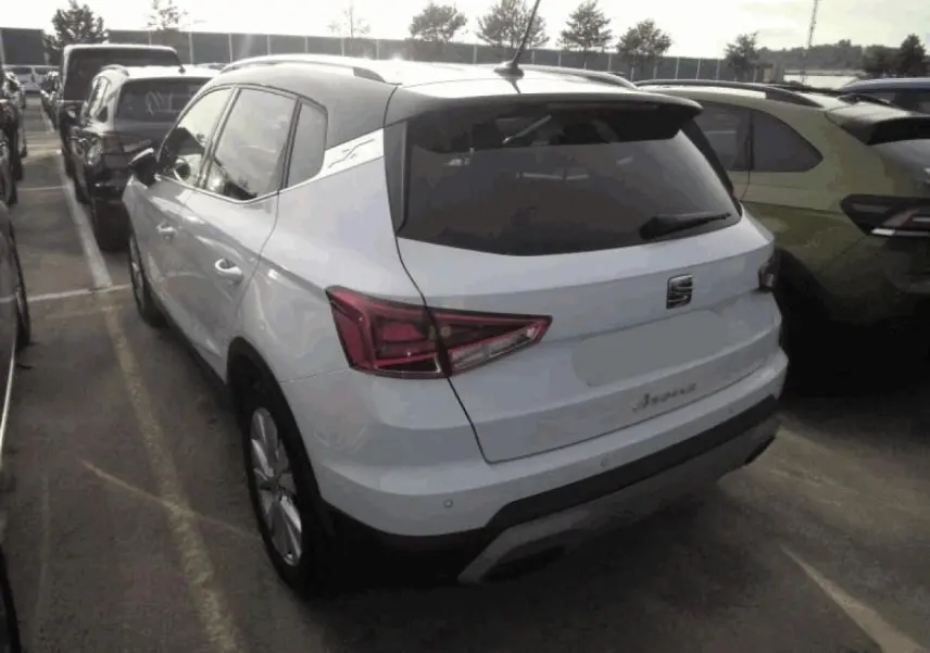 Vue 3/4 arrière d'un SEAT Arona blanc Nevada avec toit noir et feux arrière LED en triangle sur un parking.