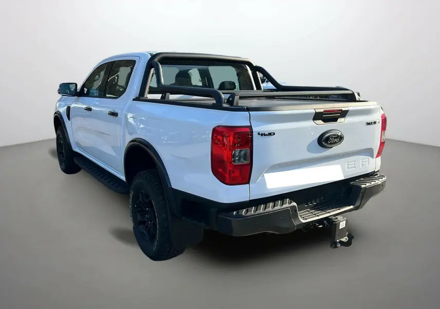 Ford Ranger blanc glacier vu 3/4 arrière droit, avec arceaux noirs et attelage visible sur fond neutre.