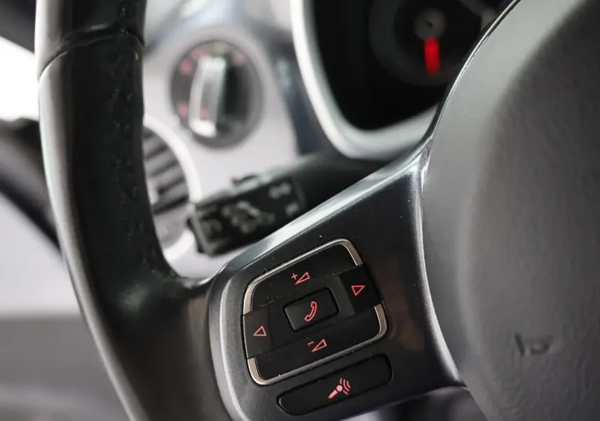 Gros plan sur les commandes au volant en cuir noir de la Volkswagen Coccinelle 2016, avec boutons rétroéclairés rouges.
