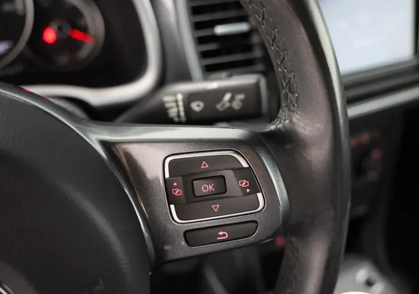 Gros plan sur les commandes au volant en cuir noir du Volkswagen Coccinelle gris, version 2016 avec GPS.
