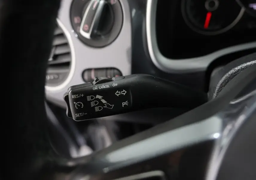 Gros plan sur la commande de régulateur de vitesse à gauche du volant dans une Volkswagen Coccinelle gris 2016.