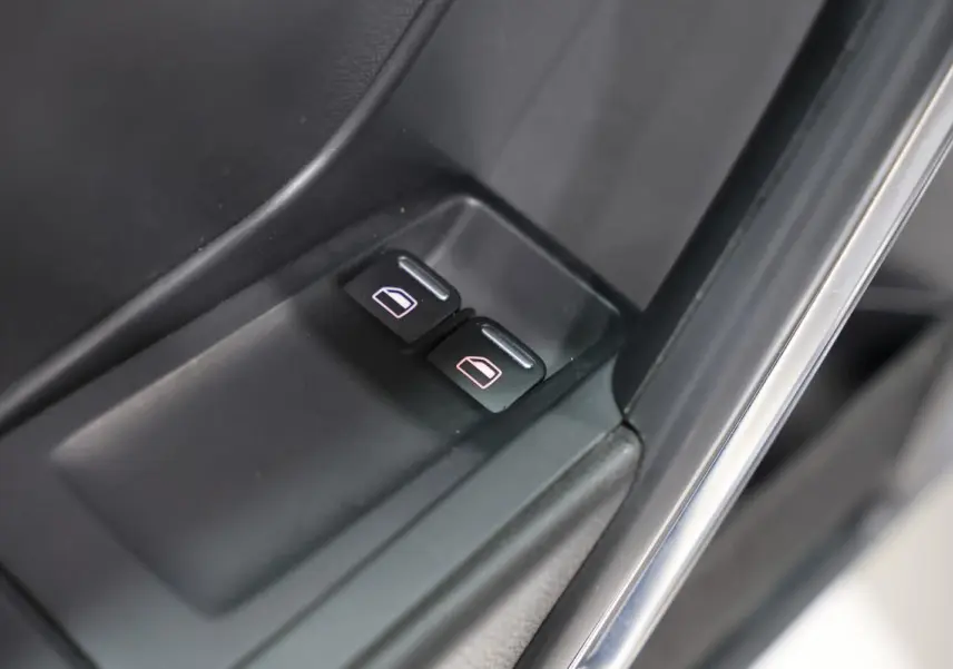 Gros plan sur les boutons de commande des vitres électriques côté conducteur d'une Volkswagen Coccinelle gris 2016.