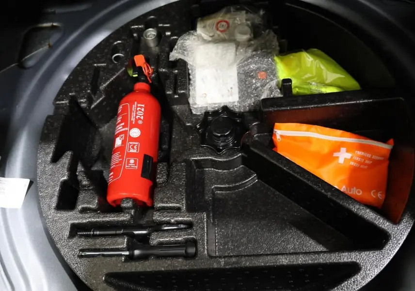 Vue plongeante sur le coffre à outils d’une Volkswagen Coccinelle gris, avec extincteur rouge et trousse de secours orange.