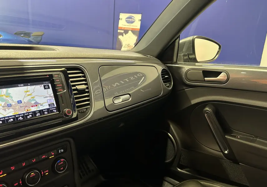 Vue intérieure côté passager du tableau de bord gris métallisé de la Volkswagen Coccinelle 2016 avec écran GPS et sellerie cuir noire.