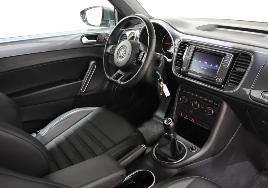 Intérieur côté conducteur de la Volkswagen Coccinelle gris 2016, volant cuir, GPS et boîte manuelle visibles.