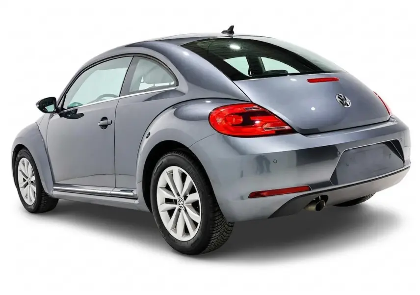 Volkswagen Coccinelle gris vue 3/4 arrière droit, avec feux arrière rouges et jantes alliage blanches.