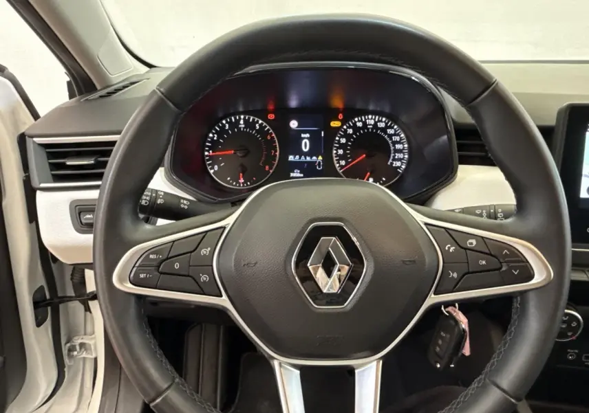 Vue intérieure centrée sur le volant cuir noir de la Renault Clio blanche avec tableau de bord numérique allumé.
