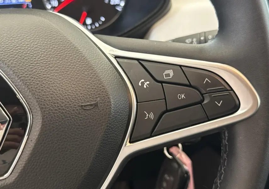 Gros plan sur le volant noir de la Renault Clio blanc 2023, avec commandes multifonctions et logo Renault visible.