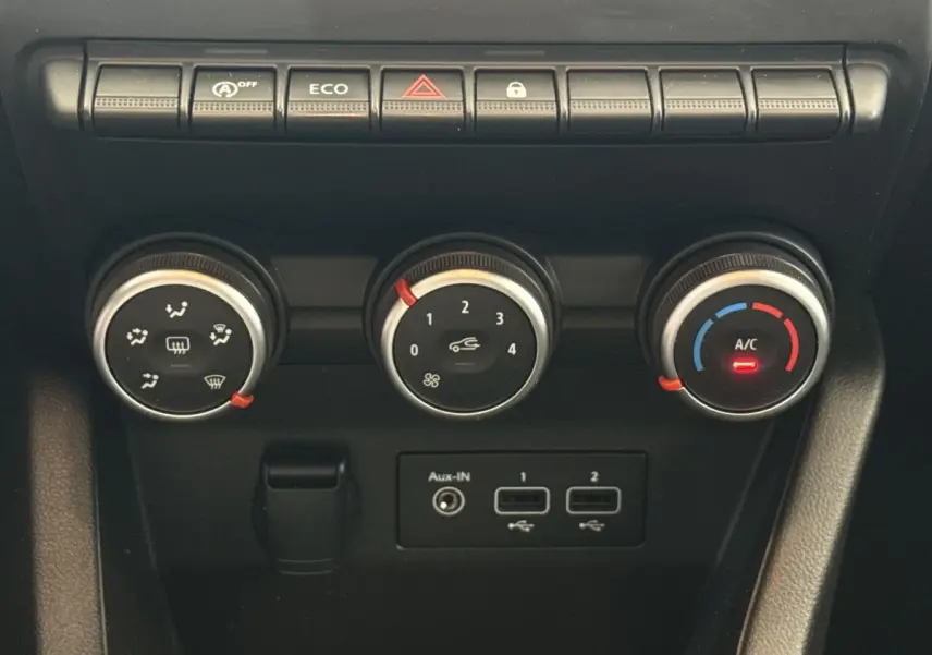 Gros plan sur les commandes de climatisation et boutons fonctionnels du tableau de bord noir de la Renault Clio blanche.