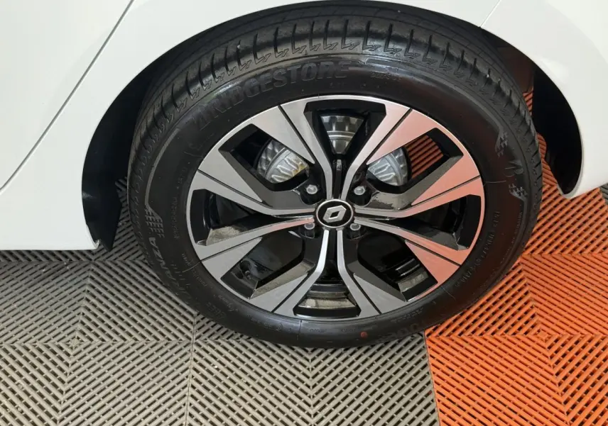 Gros plan sur la roue avant droite d’une Renault Clio blanche, jante alliage noire et argentée au design moderne.