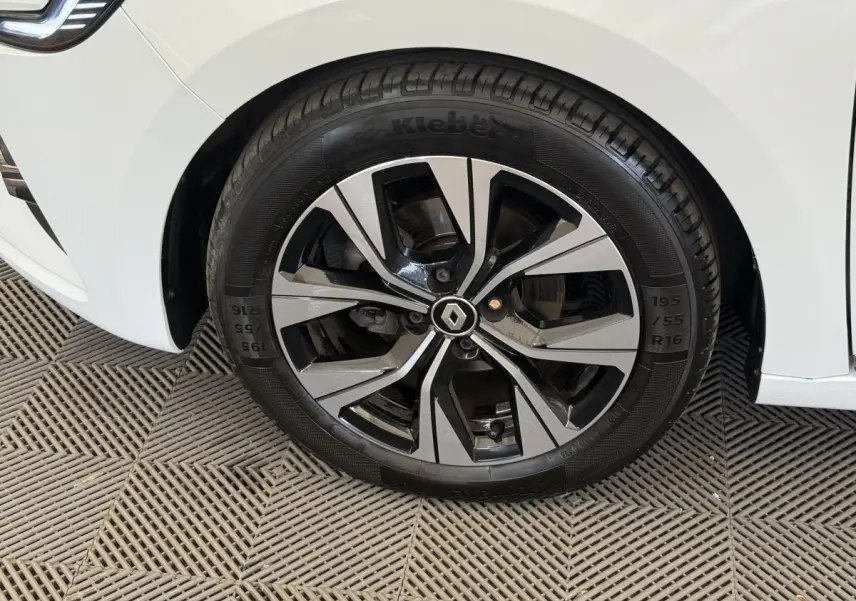 Gros plan sur la roue avant gauche d'une Renault Clio blanche avec jante alliage bicolore et logo Renault central.