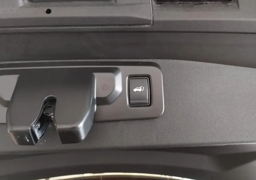 Gros plan sur le bouton d'ouverture électrique du hayon, intégré dans la garniture intérieure gris foncé du Renault Symbioz 2025.