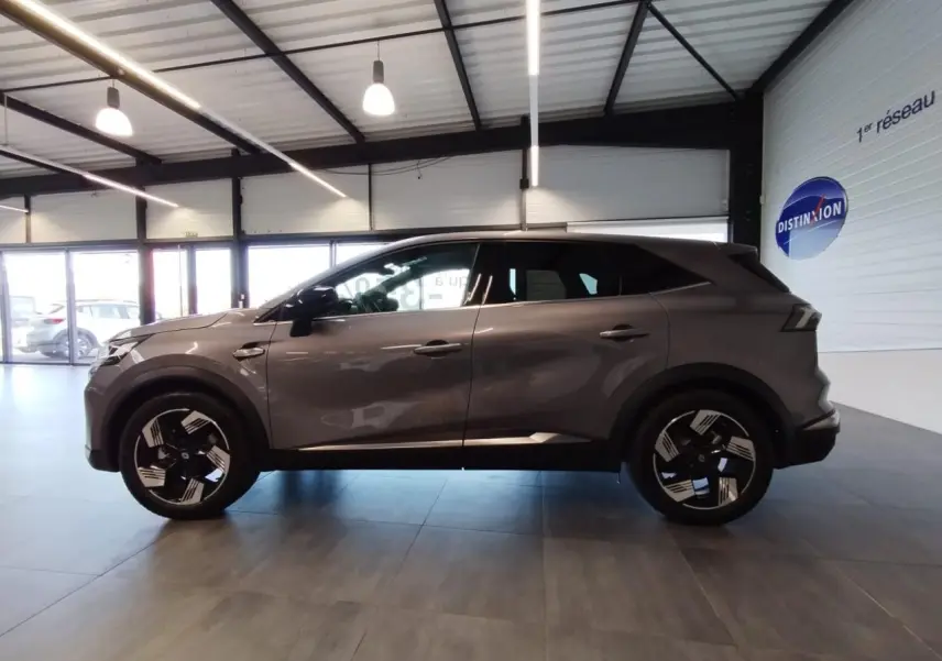Renault Symbioz 2025 gris Cassiopée vue de profil côté gauche avec jantes 18 pouces Gravity en intérieur showroom.