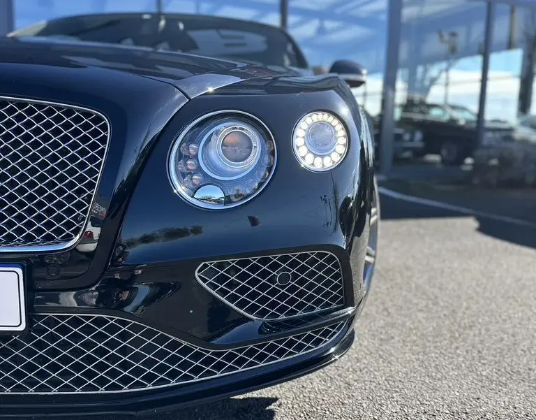 Gros plan sur l'avant droit noir brillant d'une Bentley Continental GT Speed 2015 avec ses phares ronds LED distinctifs.