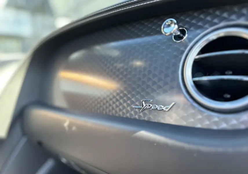 Détail intérieur du tableau de bord noir de la Bentley Continental GT Speed 2015 avec logo "Speed" et sortie d'air ronde chromée.