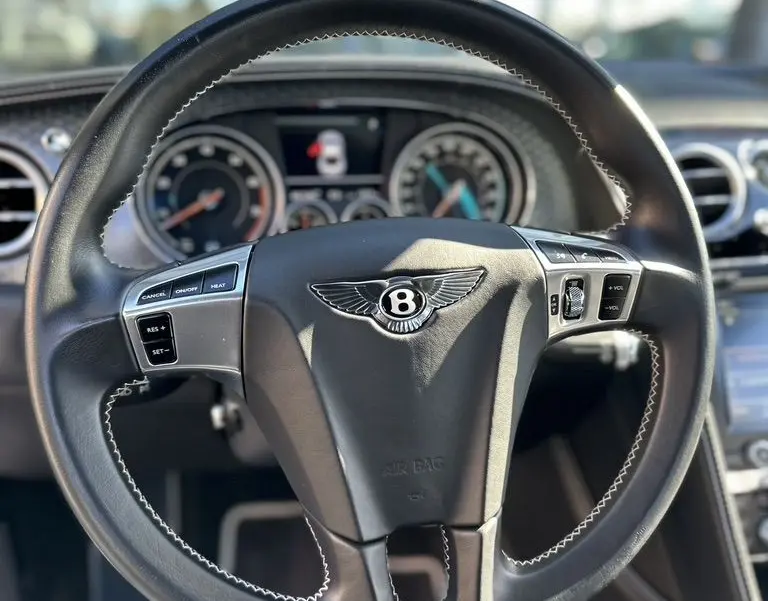 Vue rapprochée du volant noir en cuir avec logo Bentley, tableau de bord et commandes intégrées visibles à l'intérieur d'une Continental GT 2015.