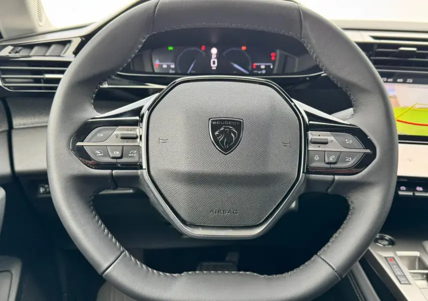 Volant cuir noir au design hexagonal du Peugeot 308 SW 2024 avec commandes intégrées et tableau de bord numérique visible.