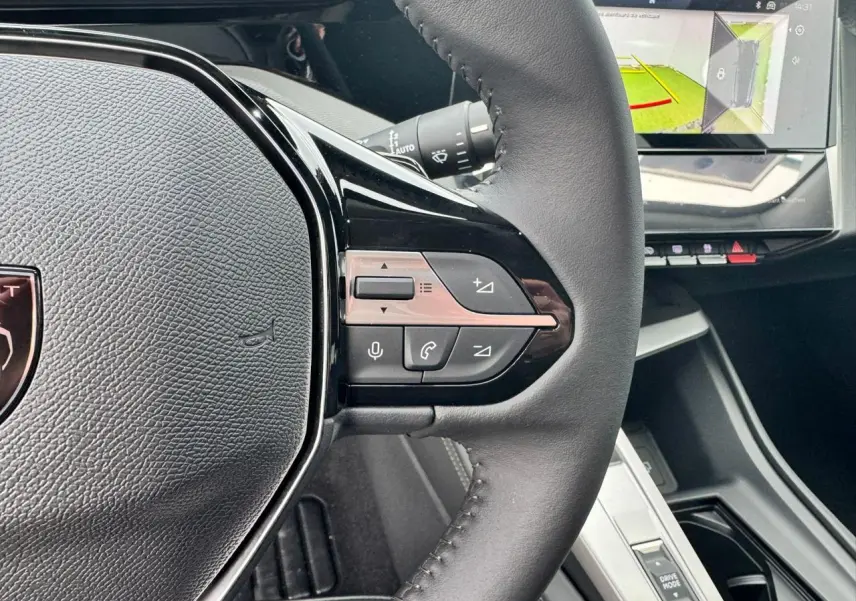 Gros plan sur le volant cuir noir de la Peugeot 308 SW 2024 avec commandes intégrées et écran tactile affichant la caméra de recul.