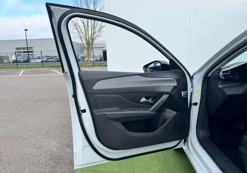 Porte avant gauche ouverte d'une Peugeot 308 SW blanche, montrant la garniture intérieure noire avec insert gris.