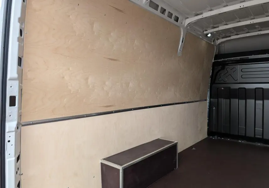 Intérieur du coffre du fourgon Iveco Daily blanc, vue latérale gauche montrant les habillages bois et plancher anti-dérapant.