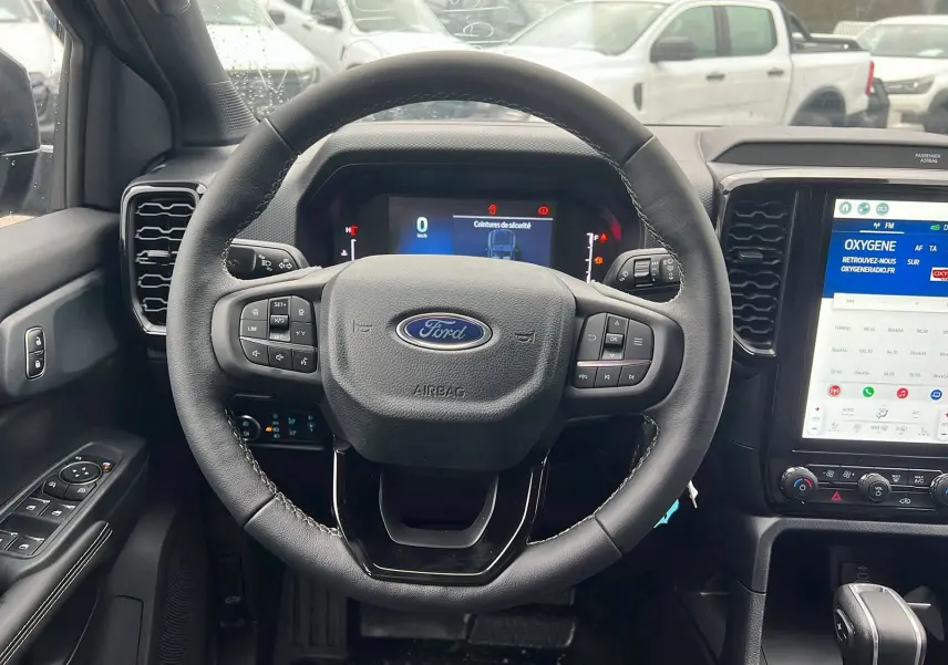 Vue intérieure centrée sur le volant cuir multifonctions et l'écran tactile vertical du Ford Ranger gris carbone 2025.