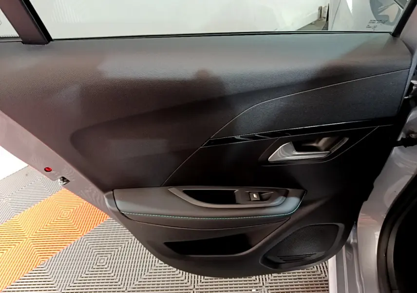 Vue rapprochée de la porte arrière droite gris clair de la Peugeot 208 avec poignée et bouton de vitre électrique.
