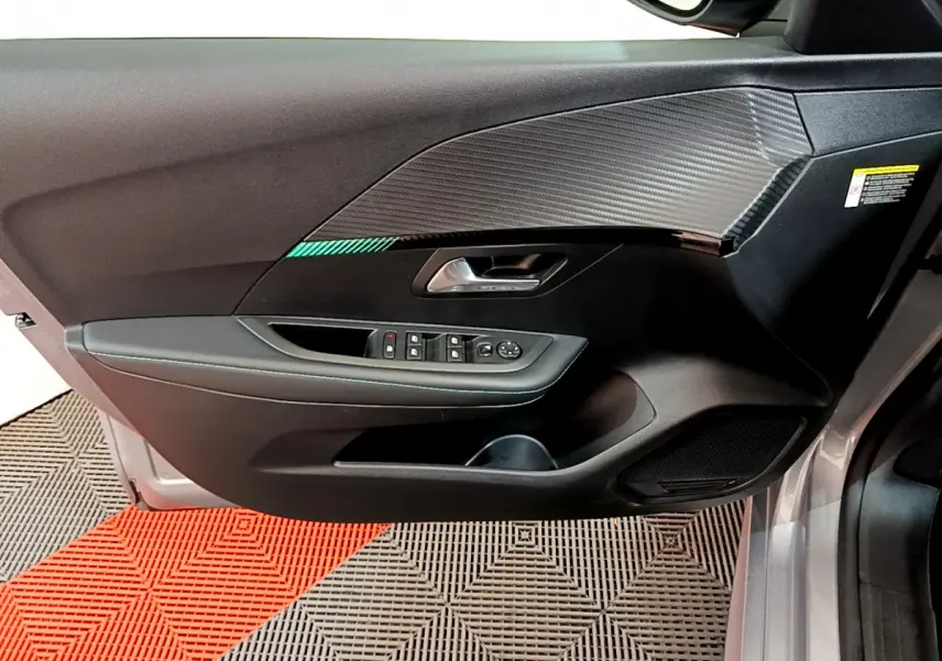 Vue intérieure côté gauche de la porte avant gris clair de la Peugeot 208 avec insert décor carbone et commandes électriques.