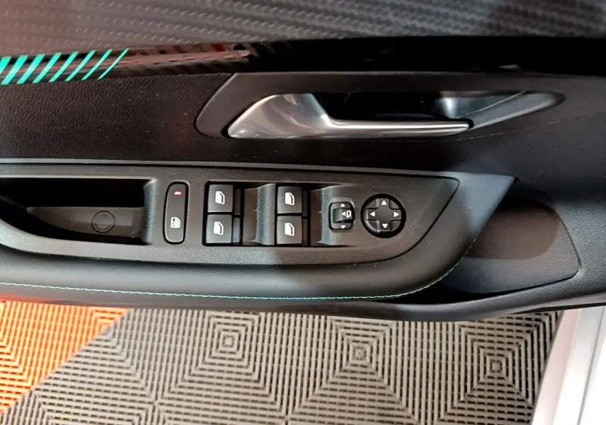 Gros plan sur la commande des vitres électriques et rétroviseurs côté conducteur d'une Peugeot 208 gris clair, porte ouverte.