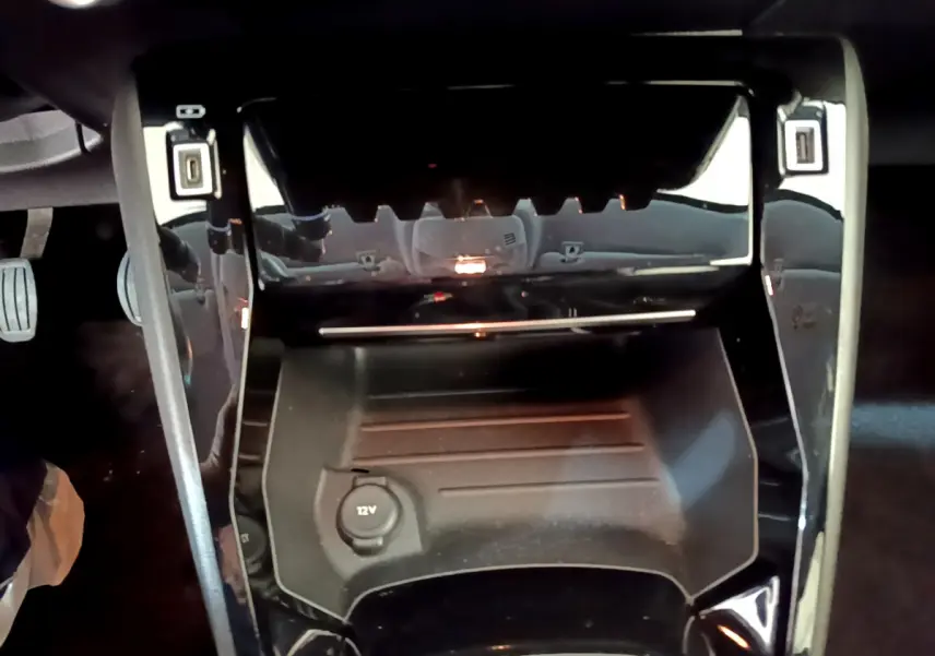 Gros plan sur la console centrale noire de la Peugeot 208 PureTech 100 S&S Allure Business avec prise 12V visible.