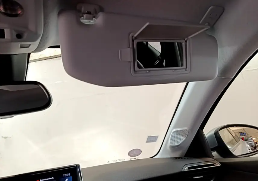 Intérieur du Peugeot 208 gris clair, vue côté passager avec pare-soleil et miroir de courtoisie ouvert.