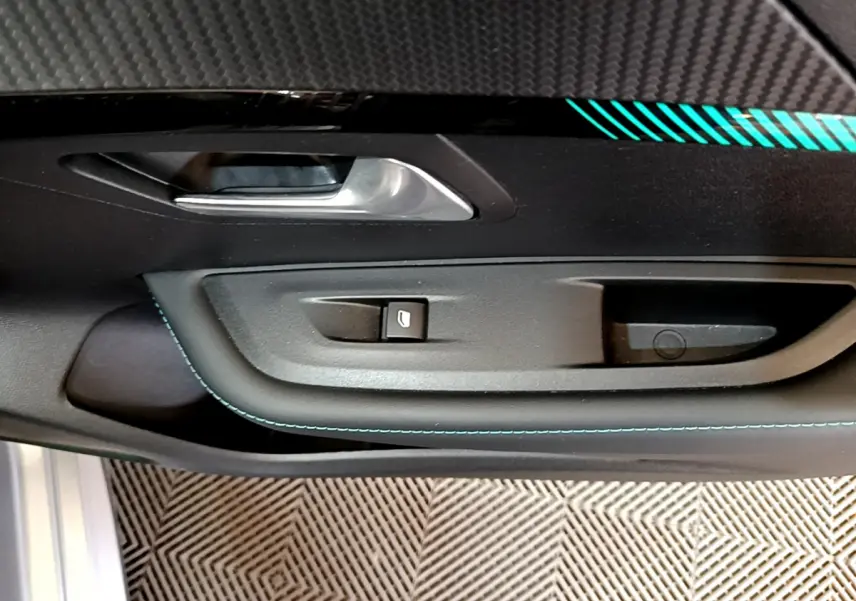 Gros plan sur la poignée intérieure et le bouton de lève-vitre côté conducteur d'une Peugeot 208 gris clair, finition Allure Business.