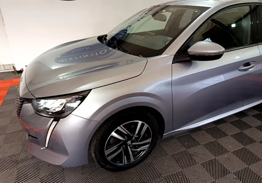 Peugeot 208 gris clair vue 3/4 avant droit, avec phares LED et jantes alliage distinctives.