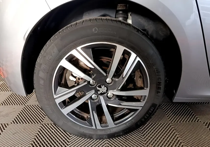 Gros plan sur la roue avant droite d'une Peugeot 208 gris clair, mettant en valeur la jante alliage noire et argentée.