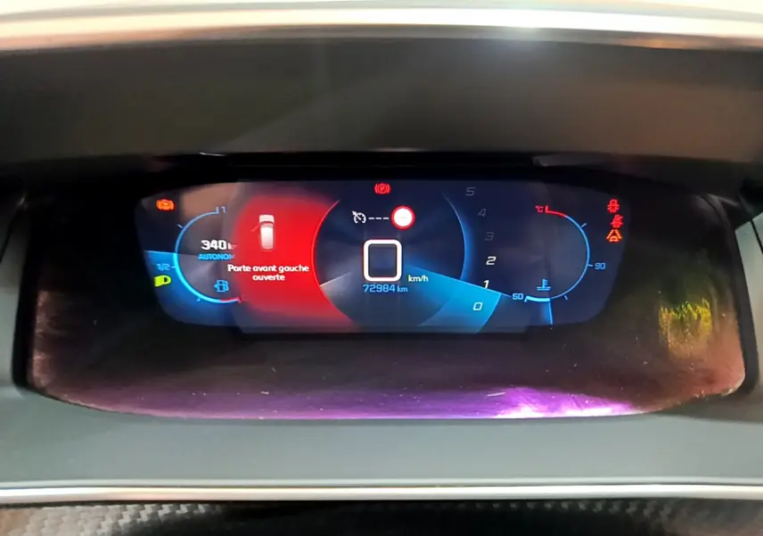Tableau de bord numérique de Peugeot 208 gris clair affichant la vitesse, autonomie et porte avant gauche ouverte.
