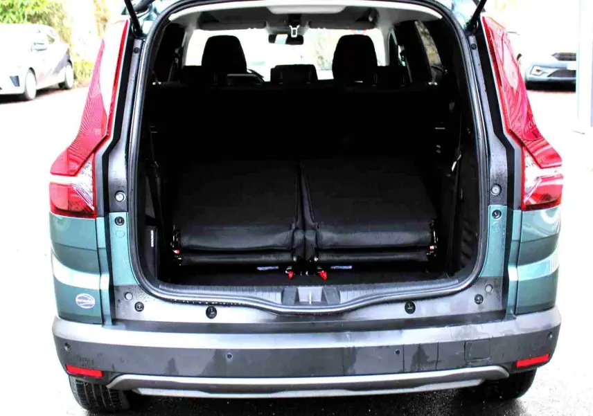 Vue arrière du Dacia Jogger vert cèdre métal avec coffre ouvert et sièges rabattus, montrant l'espace de chargement.