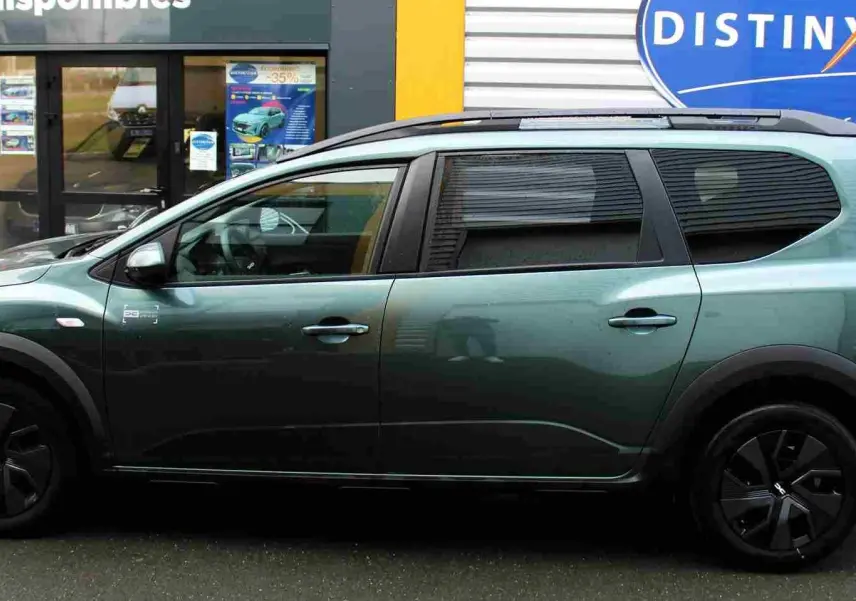 Vue de profil côté gauche d'une Dacia Jogger 2025 vert cèdre métal avec jantes noires et barres de toit.
