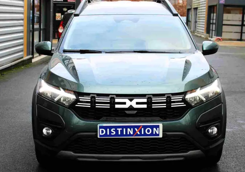 Vue avant d'un Dacia Jogger vert cèdre métal avec calandre noire et phares allumés sur fond urbain.
