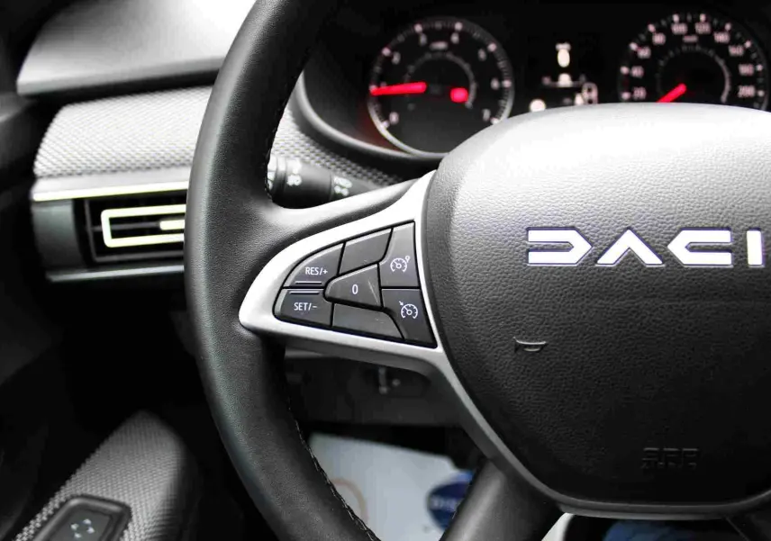 Gros plan sur le volant noir de la Dacia Jogger 2025, avec commandes intégrées et tableau de bord en arrière-plan.
