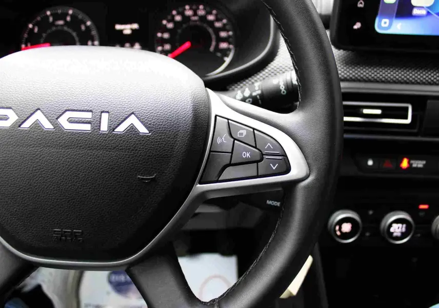 Gros plan sur le volant noir de la Dacia Jogger 2025 avec commandes multifonctions et tableau de bord en arrière-plan.