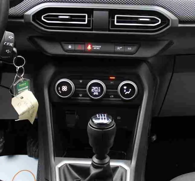Vue intérieure centrée sur la console centrale d'une Dacia Jogger 2025, avec écran tactile, commandes climatisation et levier de vitesse manuel.