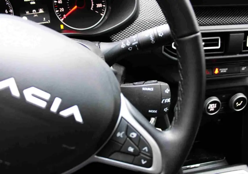 Gros plan sur le volant noir en cuir de la Dacia Jogger 2025, avec commandes intégrées et tableau de bord partiellement visible.