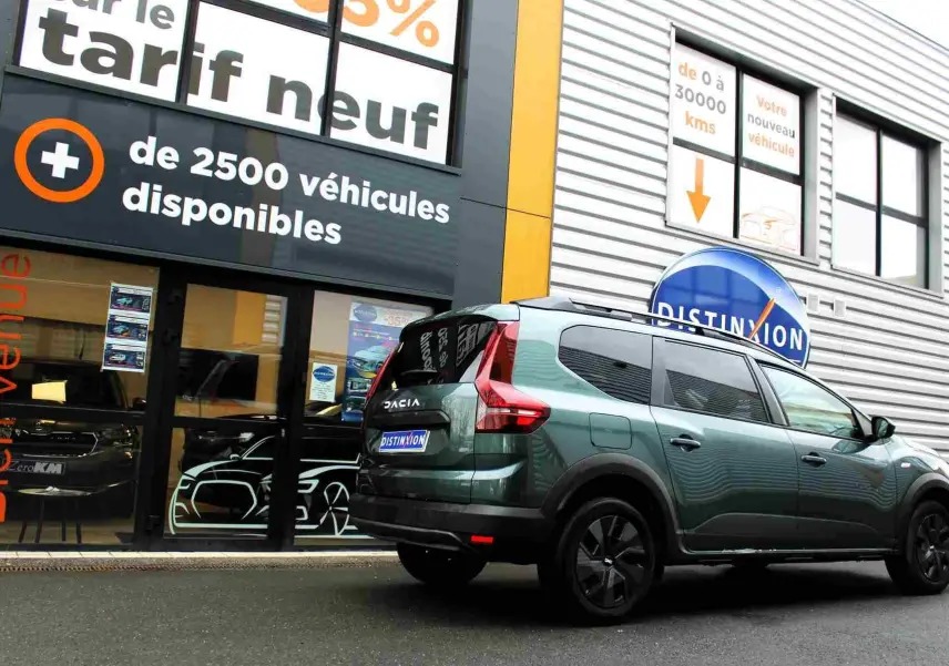 Vue 3/4 arrière droite d'un Dacia Jogger vert cèdre métallisé avec vitres teintées, garé devant un showroom.
