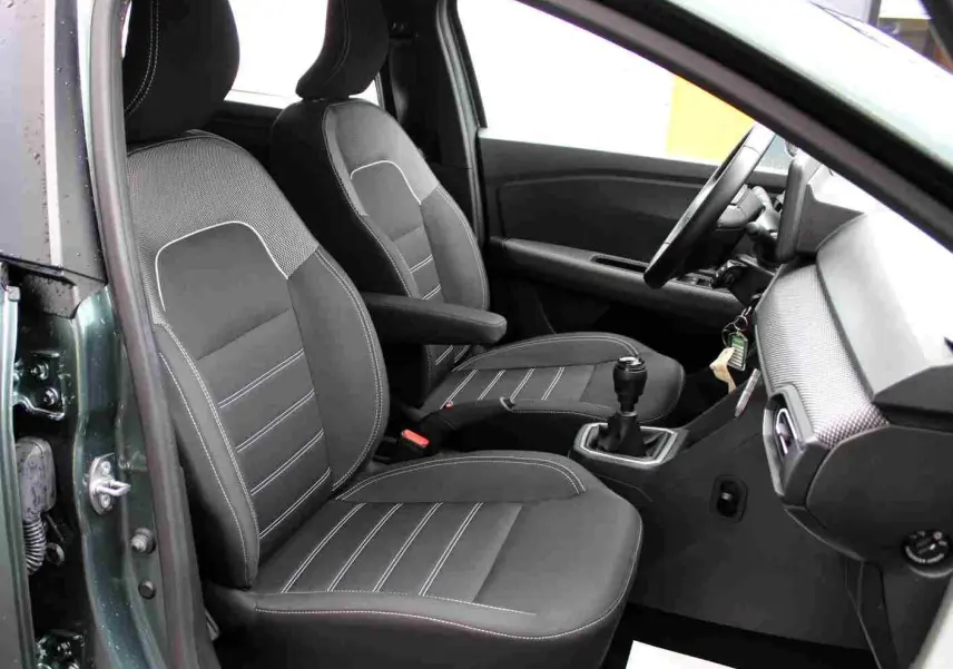 Vue intérieure côté gauche du Dacia Jogger 2025 vert cèdre, montrant les sièges avant noirs et la boîte manuelle.