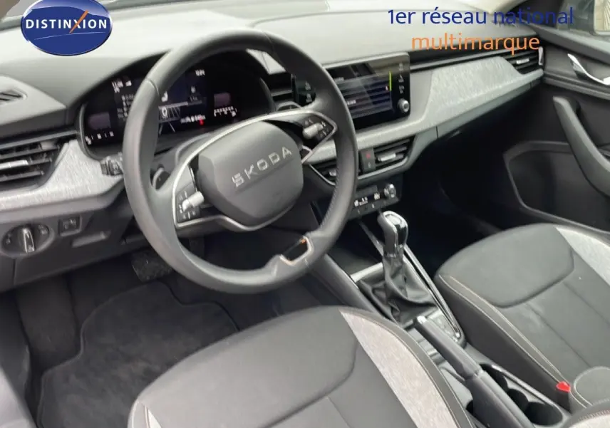 Vue intérieure côté conducteur du Skoda Kamiq 2025, volant multifonction, sièges tissu noir et gris, console centrale avec boîte auto.